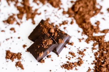 Close up view of chocolate pieces with dry cocoa on white background.