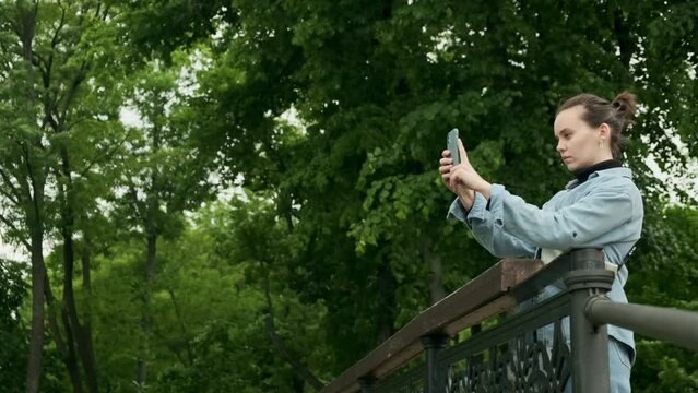 Girl takes pictures on smartphone. Female traveler taking photos with mobile camera in the park. Young woman tourist shoots the sights.