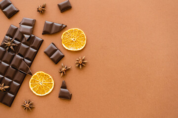 Top view of dark chocolate, dry orange slices and anise spice on brown background.