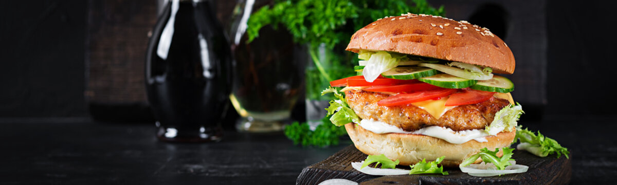 Hamburger with chicken burger meat, cheese, tomato, cucumber and lettuce on wooden background. Tasty burger. Banner. Close up