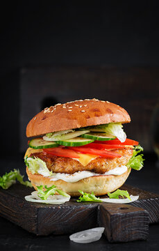 Hamburger with chicken burger meat, cheese, tomato, cucumber and lettuce on wooden background. Tasty burger. Close up