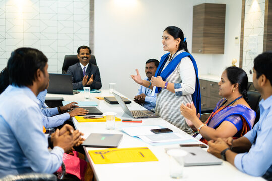 woman employee speaking confidently at board meeting in front of cowrkers - concept of briefing strategy, business planning and leadership