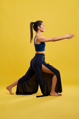 Yogi girl with ponytail keeping arms stretched, while staying in yoga pose indoor. Side view of fit...