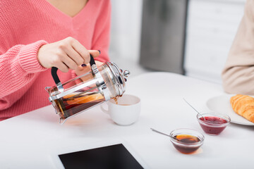 cropped view of woman pouring tea near digital tablet with blank screen.