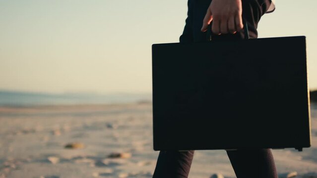 Businessman with black briefcase walks in the beach near the sea.