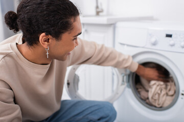 happy african american man putting clothes in washing machine.