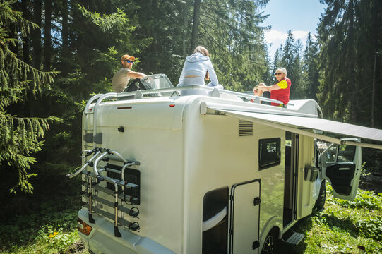 Caucasian Family Of Three Hanging Out On A Motorhome Roof During Their Vacation Road Trip. Relaxing And Socializing On A Camping. Outdoors And Recreation Theme.