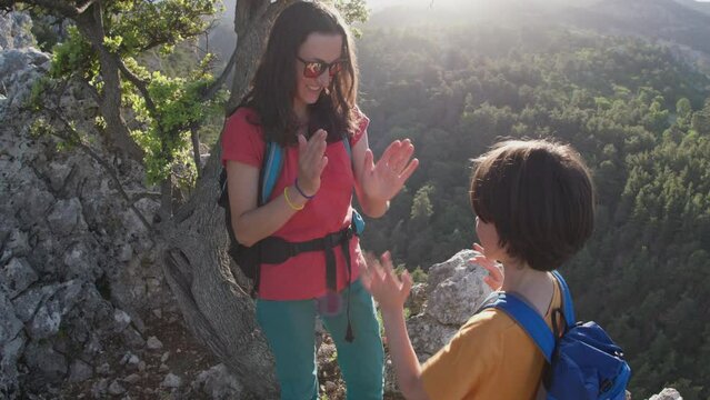 A woman with a child on a mountain top, a mother plays with her son, a boy with a backpack travels with his mother, a hike in the mountains with children, okey-dokey