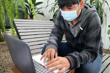 Masked Asian man working online in shady shop off-site work concept