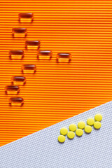 flat lay of yellow pills on and jelly capsules on white and orange textured background.