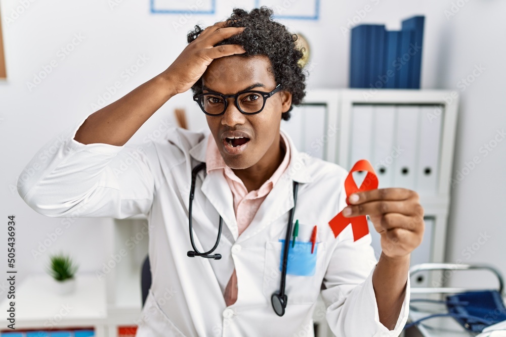 Sticker African doctor man holding support red ribbon stressed and frustrated with hand on head, surprised and angry face