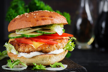 Hamburger with chicken burger meat, cheese, tomato, cucumber and lettuce on wooden background. Tasty burger. Close up