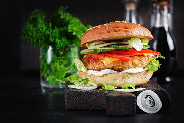 Hamburger with chicken burger meat, cheese, tomato, cucumber and lettuce on wooden background....