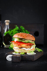 Hamburger with chicken burger meat, cheese, tomato, cucumber and lettuce on wooden background. Tasty burger. Close up