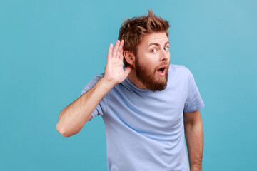 Fototapeta Can't hear you. Portrait of attentive bearded man holding hand near ear trying to listen quiet conversation, overhearing gossip, having hearing problems. Indoor studio shot isolated on blue background obraz