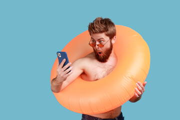 Portrait of astonished surprised bearded man in sunglasses standing with orange rubber ring and...