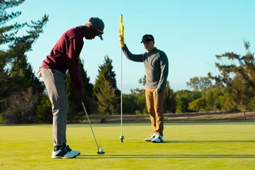 Gordijnen African american young man playing golf with caucasian friend against clear sky at golf course © wavebreak3