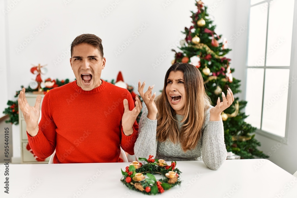 Canvas Prints Young hispanic couple sitting at the table on christmas crazy and mad shouting and yelling with aggressive expression and arms raised. frustration concept.