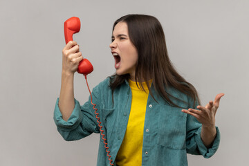 Portrait of aggressive young adult dark haired woman screaming while talking phone, displeased with...