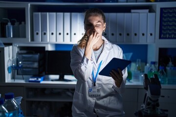 Beautiful blonde woman working at scientist laboratory late at night smelling something stinky and...