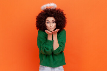 Angelic woman with Afro hairstyle wearing green casual style sweater and nimbus over head sending...