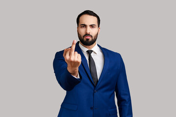 Portrait of strict serious rude bearded man looking at camera and showing middle finger, expressing negative emotions, wearing official style suit. Indoor studio shot isolated on gray background.