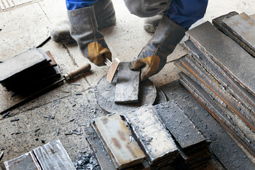 Worker in heavy industry or metallurgy beats scale off iron plates with hammer. Work with metal....