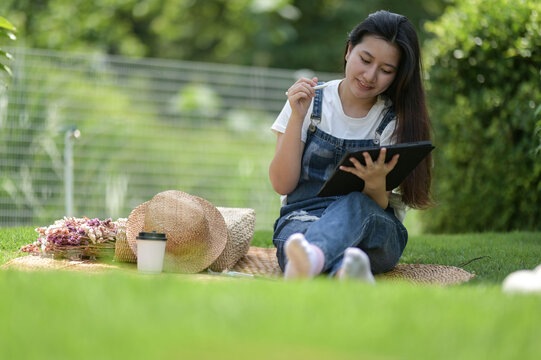 Young woman relaxing in the lawn and using a tablet. Tablet with pen in hand.
