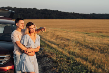 Cheerful Young Couple Hugging Near the Car, Caucasian Woman and Man Enjoying Road Trip at Sunset, Copy Space