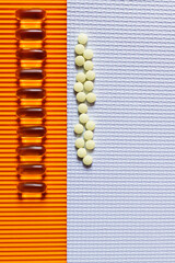 flat lay of rows with yellow pills on and jelly capsules on white and orange textured background.