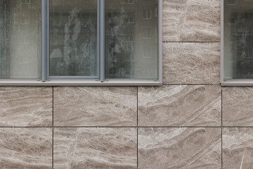 Wall with window of rectangular smooth brown tiles with rock slab texture. Stone street covering of...