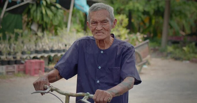 A happy smiling Asian male farmer who is the long life native 98 years, white hair, freckled skin, still in good health, standing with his old bicycle, living in a rural farmer's village.
