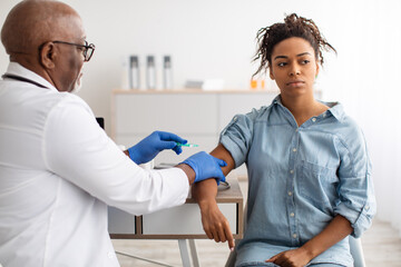 Black Woman Receiving Vaccine Injection Sitting With Doctor Indoor