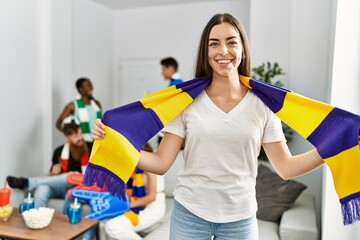 Young soccer hooligan woman smiling happy holding team scarf at home