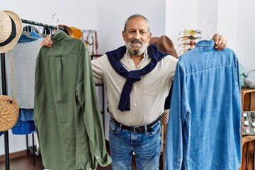 Senior grey-haired man smiling confident holding shirt at clothing store