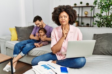 Mother of interracial family working using computer laptop at home thinking concentrated about...