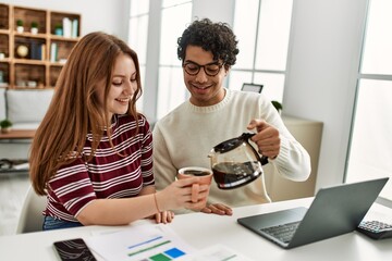 Young couple using laptop and pouring coffee sitting on the table at home.