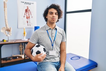 Hispanic man with curly hair working as football physiotherapist puffing cheeks with funny face....