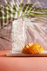 tall cocktail glass filled with uneven ice cubes and cut in cubes mango half on tropical palm tree background, gobo mask effect