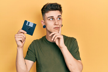 Young caucasian boy with ears dilation holding floppy disk serious face thinking about question...