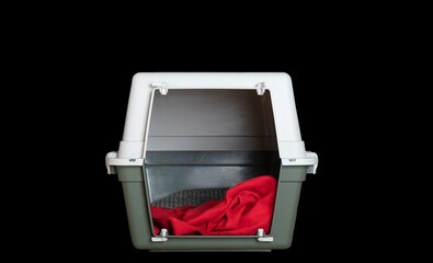 On a black background in the studio there is a special large plastic container for transporting animals, with a red soft blanket inside.