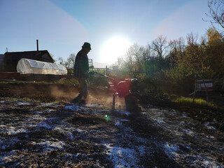 elderly pensioner man plows the ground with a tillerblock in the garden. Man farmer working in...