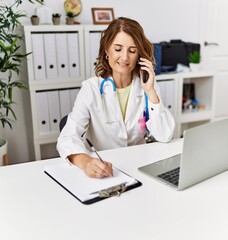 Middle age hispanic woman wearing doctor uniform talking on the smartphone at clinic