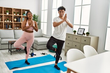 Fototapeta premium Young latin couple smiling happy training yoga pose at home.