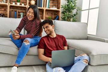Young latin couple smiling happy using laptop and smartphone at home.