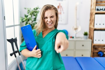 Young caucasian woman working at pain recovery clinic pointing displeased and frustrated to the camera, angry and furious with you