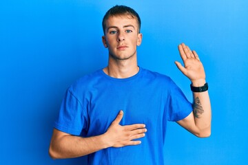 Young caucasian man wearing casual blue t shirt swearing with hand on chest and open palm, making a loyalty promise oath