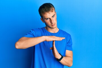 Young caucasian man wearing casual blue t shirt doing time out gesture with hands, frustrated and...