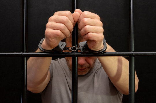 A man in handcuffs in a cell behind bars. Concept: a prisoner in a courtroom, a court sentence to a convicted person, a prison term.