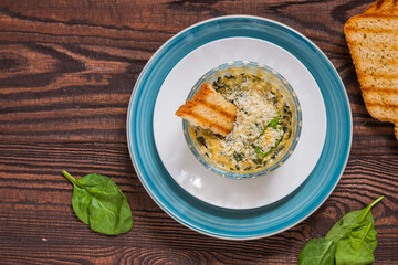 Hot appetizer, spinach and cream cheese dip in a transparent form on a blue plate on a brown wooden background. Served with toasted wheat bread.